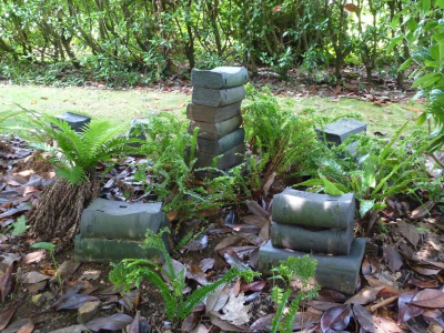 Escultura de Caxigueiro consistente en varias pilas de libros de cerámica oscura. Están colocados en el jardín rodeados de helechos
